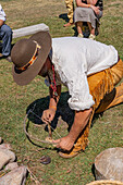 A man in period dress demonstrates using a bow & drill to start a fire at the Fort Bridger Mountain Man Rendezvous in Wyoming.