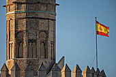 The Spanish flag flutters above Torre del Oro, a historic watchtower symbolizing Seville's maritime history beside the Guadalquivir River.