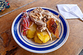 Traditional hornado or roasted pork & llapingacho potato pancakes at a street eatery in Otavalo, Ecuador.