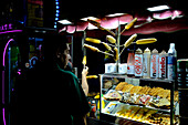 A man in front of a street food stall during the Virgin of La Paloma festivities at night in Madrid, Spain