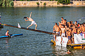 Seville, Spain, July 24 2012, A contestant tries to maintain balance while attempting cucaña during the Velá festival in Triana, Seville, showcasing skill and tradition.