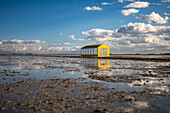 A bright yellow granary emerges from the flooded rice fields of Isla Mayor after harvest, reflecting against the water under a blue sky.
