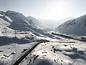 Aerial view of snowy mountains and a winding road under clear sky, Julierpass, Grisons, Switzerland.