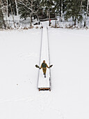Aerial view of a snowy Labanoras forest with a serene bridge and a solitary person walking through the tranquil landscape, Svencionys, Lithuania.