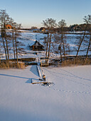 Aerial view of Visbaras lake in winter with frozen surface, cabin, and trees, Moletai, Lithuania.