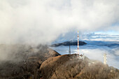 Luftaufnahme des schneebedeckten Montevergine mit einer Antenne inmitten von Wolken und Nebel, Mercogliano, Avellino, Italien.