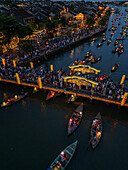 Aerial view of a vibrant river scene with boats and illuminated bridges casting a warm glow over the Thu Bon River, H?i An, Qu?ng Nam, Vietnam.
