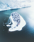 Aerial view of a snow-laden island oasis, its frosted trees contrasting against the icy waters, creating a serene winter landscape, Lake Nojiri, Nagano, Japan.