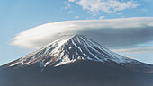 Blick auf den majestätischen Berg Fuji, dessen Gipfel von einer markanten linsenförmigen Wolke gekrönt wird, die sich gegen den klaren blauen Himmel abhebt, Fujikawaguchiko, Yamanashi, Japan.