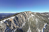 Aerial view of the striking Rote Wand mountain under a clear blue sky, snow dusting its rugged slopes, a stunning contrast of textures, Frohnleiten, Steiermark, Austria.
