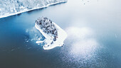 Aerial view of a snow-dusted island in the middle of a calm, glassy lake reflecting the serene winter sky, Lake Nojiri, Nagano, Japan.