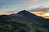 Luftaufnahme des majestätischen Berges Teide, der sich aus der Vulkanlandschaft erhebt, unter einem Himmel in Orange- und Blautönen, Teneriffa, Kanarische Inseln, Spanien.