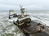 Aerial view of the Zeila shipwreck's decaying metal structure amidst the turbulent, foamy waves of the Skeleton Coast, Zeila shipwreck, Erongo Region, Namibia.