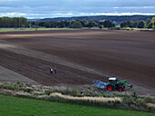 Luftaufnahme eines Traktors auf einem bepflanzungsbereiten Feld in der Nähe der Stadt Bralitz, in der Nähe stehen zwei Figuren, Bad Freienwalde, Brandenburg, Deutschland.