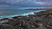 Aerial view of volcanic coast with waves and a woman in a yellow jacket, Lanzarote island, Canary Islands, Spain.