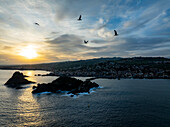 Aerial view of beautiful sunset over tranquil sea with birds and island along picturesque coastline, Aci Castello, Catania, Italy.