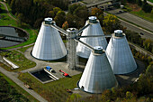 Aerial view of modern sewage treatment plant with conical structures surrounded by greenery and trees, Schwabing-Freimann, Bayern, Deutschland.