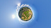 Aerial view of a tiny planet perspective of a serene village surrounded by beautiful fields under a blue sky with clouds and sunlight, Safnern, Bern, Switzerland.