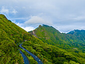 Luftaufnahme von üppig grünen Bergen und einer kurvenreichen Autobahn inmitten einer malerischen Waldlandschaft, Kaneohe, Hawaii, Vereinigte Staaten.