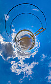 Aerial view of a tiny planet perspective featuring a vibrant suspension bridge under a blue sky with clouds, Hessle, England, United Kingdom.
