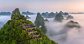 Luftaufnahme einer Aussichtsterrasse auf dem Berggipfel mit Blick auf die Berglandschaft von Guilin bei Sonnenaufgang mit tief hängenden Wolken, Guangxi, China.