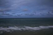 Aerial view of dark waters meet the shore under a brooding, cloudy sky, the ocean's surface a canvas of blurred motion and muted tones, Miami Beach, Florida, United States.