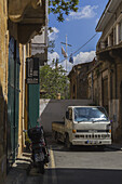 Lefkosia, Cyprus - 25 June 2025: View of a narrow street scene with a white truck parked beside an old stone building, under a bright sky with flags fluttering above.