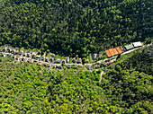 Luftaufnahme von Häusern inmitten dichter grüner Wälder, die zu Tennisplätzen und einem Gebäude führen, wodurch ein lebhafter Kontrast zwischen Natur und Struktur entsteht, Thann, Grand Est, Frankreich.