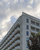 View of a modern building with balconies reaching towards a cloudy sky, captured in a ground-level perspective, Ayia Napa, Ammochostos, Cyprus.