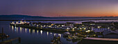 Aerial view of the city's fish port at dawn, where the lights of the Sealord factory site reflect on the water, contrasting with the dark silhouettes of distant mountains, Nelson, Nelson Region, New Zealand.