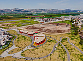 Luftaufnahme von leuchtend roten und gelben Gebäuden in einem Park mit verschlungenen Wegen, die sich von den Bergen in der Ferne abheben, Afula, Nordbezirk, Israel.