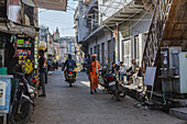 Pushkar, India - 24 June 2025: View of the vibrant street scene with people walking and riding motorbikes amidst the old buildings, capturing the essence of Pushkar's spiritual and urban life..