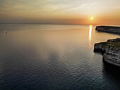 Luftaufnahme der Klippen und des ruhigen Meeres bei einem goldenen Sonnenuntergang, der den Himmel in Orange- und Bernsteintönen färbt, Munxar, Munxar, Malta.