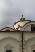 Blick auf die cremefarbene Steinkirche mit ihren eleganten Bögen und der Kuppel, die sich in den wolkenverhangenen Himmel reckt, eine ruhige Szene in Pano Lefkara, Larnaca, Zypern.