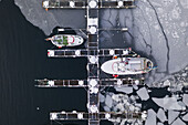 Luftaufnahme von Fischerbooten, die an einer Anlegestelle inmitten eines faszinierenden Mosaiks von Eisschollen festgemacht sind, wo das dunkle Wasser auf das weiße Eis trifft, Svolv?r, Nordland, Norwegen.