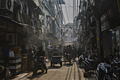 New Delhi, India - 24 June 2025: View of a bustling street scene with scooters, rickshaws, and pedestrians amidst a maze of overhead wires and aged buildings.