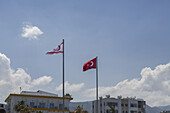 Aerial view of two flags waving gently against the blue sky, one Turkish and one Northern Cyprus, shimmering under the sun, Kyrenia, Cyprus.