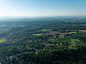Luftaufnahme eines dichten, lebendigen Waldes, der von landwirtschaftlichen Feldern durchsetzt ist, die unter einem klaren Himmel einen Teppich aus Grün und Braun bilden, Zillisheim, Grand Est, Frankreich.