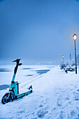 View of a turquoise scooter rests in the deep snow, illuminated by the soft glow of streetlights on a cold winter night, Reykjavík, Reykjavíkurborg, Iceland.