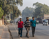 Agra, India - 24 June 2025: View of three men strolling along a sun-drenched street, their vibrant clothing a stark contrast to the muted tones of the surrounding urban landscape.