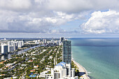 Luftaufnahme der Küstenlinie, wo moderne Wolkenkratzer auf den ruhigen türkisfarbenen Ozean treffen und einen atemberaubenden Kontrast zum klaren Himmel bilden, Sunny Isles Beach, Florida, Vereinigte Staaten.
