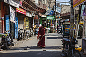 Bikaner, India - 24 June 2025: View of a vibrant street scene unfolds with a woman in a red sari amidst the bustling shops and parked vehicles.