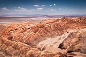 View of rugged, sun-baked peaks and valleys carve a dramatic landscape under a vast sky, showcasing the stark beauty of the arid terrain, San Pedro de Atacama, Antofagasta, Chile.