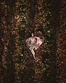 Aerial view of a woman lying in a field with green plants creating a striking contrast against the dark soil, Gialtra, Evia, Greece.
