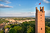 Aerial view of a medieval brick tower standing tall, topped with a vibrant red flag, overlooking a Tuscan landscape bathed in soft sunlight, San Miniato, Tuscany, Italy.