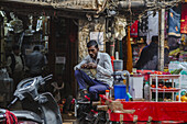 New Delhi, India - 24 June 2025: View of a man perched amidst the vibrant chaos of a market stall, where the cool steel of a scooter meets the warm hues of oranges and textiles.