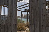 View of decaying wooden structure framing the ghostly silhouette of distant buildings across shimmering waters, a poignant scene, Varosha, Famagusta, Cyprus.