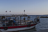 Blick auf ein rot-weißes Fischerboot, das friedlich im Hafen liegt und das sanfte Licht der Abenddämmerung auf dem ruhigen Wasser reflektiert, Dipkarpaz, Nordzypern, Cipro.