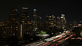 Los Angeles, United States - 25 June 2025: Aerial view of a vibrant city skyline ablaze with golden lights, streaked by the blurred trails of passing cars on the freeways.