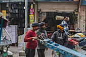 New Delhi, India - 24 June 2025: View of men gathered by a blue cart outside a shop stacked with books, capturing the vibrant street life and commerce of the city.